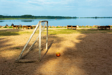 Soccer goal and ball on the beach. Sunlight, water and sand. The beach on the lake of the tourist base.