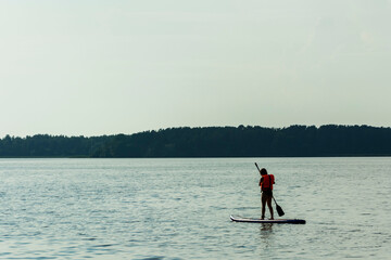 Fototapeta na wymiar A young mother swims on a standing paddle board . SUP board. Water sports