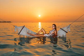 Beautiful sexy bikini woman silhouette on hammock posing in the Indian ocean on sunset, maldivian romantic scenery. Sunset on Maldives. Maldives landscape.