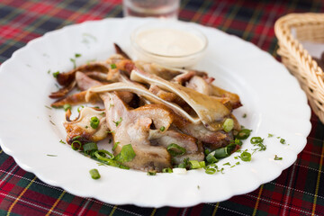 delicious smoked pork ears served with sour cream and herbs on a white plate in a restaurant