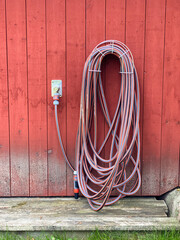 Garden hose on hanger on red wood wall.