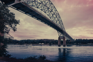 Rugged twilight seascape under Bourne Bridge at Cape Cod Canal with a speed boat passing.