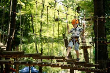 Rope park for children. A young boy in a flap climbs obstacles. Active sports recreation of the child.
