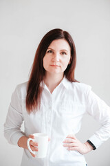 Beautiful woman in a white shirt holding a white ceramic cup on a white background. Woman drinking water coffee tea from white mug cup. Copy, empty space for text