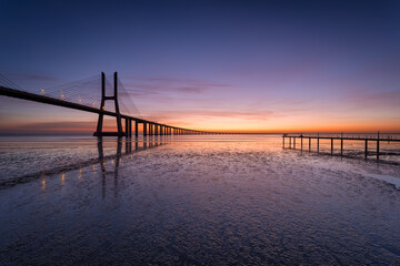 Fototapeta na wymiar Vasco da Gama bridge over tagus river and a pier before sunrise in Lisbon, Portugal.