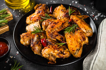 Grilled chicken wings with spices and tomato sauce at black table. Close up