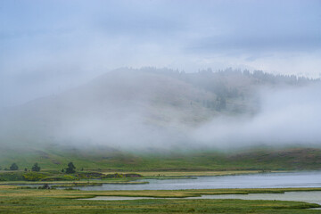 picturesque view of lake near hill in foggy morning 