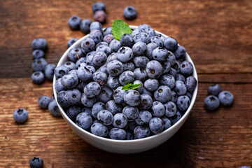 Fresh blueberries in a bowl on a brown wooden background.