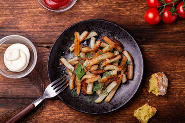Fried potatoes on a plate with herbs on a wooden background. Ketchup, mayonnaise and bread lie side by side.