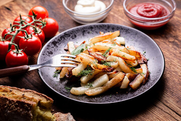 Delicious fried chopped potatoes with ketchup, mayonnaise and herbs on a wooden background.