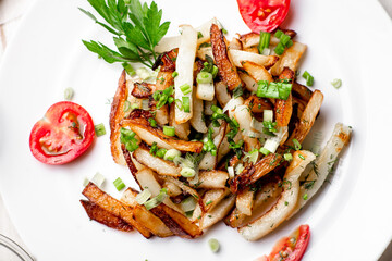 Fried potatoes in a white plate with green onions, parsley, tomatoes on a white wooden background.