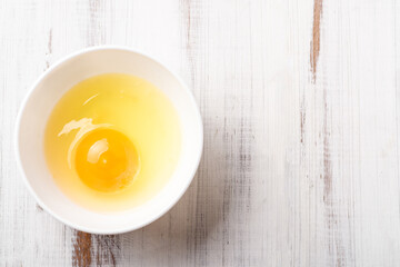 Raw egg in a plate on a white wooden background.
