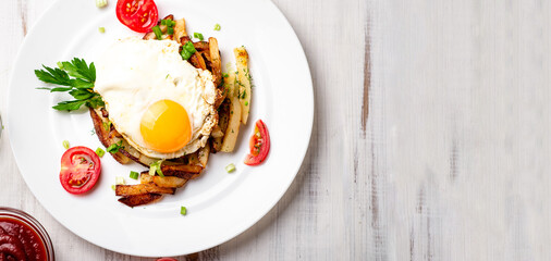 Fried potatoes with egg, herbs and tomatoes on a white plate on a white wooden background.