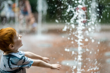 Young boy in the summer fountain in the park. Summer vacation time.