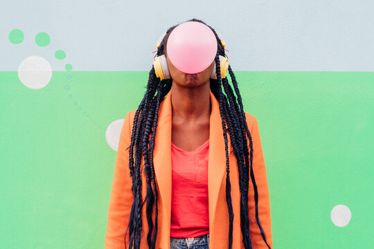 Italy, Milan, Stylish woman with headphones blowing gum against wall