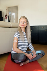 Austria, Vienna, Senior woman with adhesive bandage on arm sitting on yoga mat