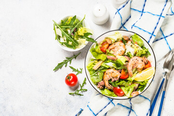 Seafood salad with fresh salad leaves, tomatoes and shrimps. Top view at white table.