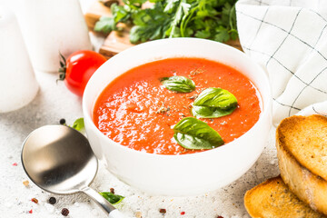 Tomato soup with basil at white table. Summer cold vegan dish.