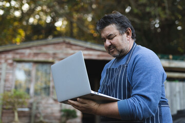 Portrait of caucasian male gardener using laptop at garden centre