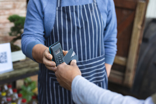 Midsection of two diverse men using contactless payments at garden centre - Powered by Adobe