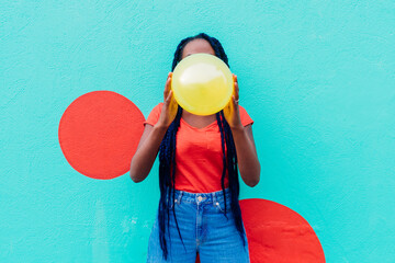 Italy, Milan, Young woman with braids blowing yellow balloon