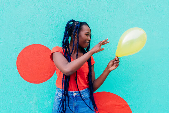 Italy, Milan, Young woman with braids holding yellow balloon