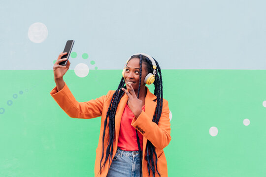 Italy, Milan, Stylish woman with headphones holding smart phone in front of wall