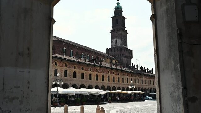 Vigevano, Lombardy, Italy. July 2021. A tourist is photographing the tower of the Sforza castle in piazza del duomo with her smartphone. Point of view upon entering the square. Beautiful summer day.