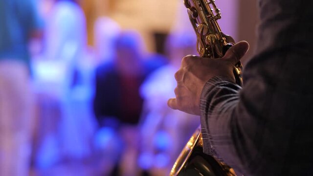 Saxophonist. Male hands are holding saxophone, saxophone player push saxophone buttons and plays melody in bright banquet hall. Close-up