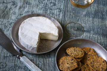 High angle selective focus view of goat cheese on small metal plate, with knife, crackers and small...