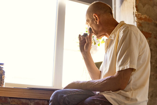Mature or senior painter or artist with graphite crayon in front of camera. Man in a paint-stained shirt working at studio