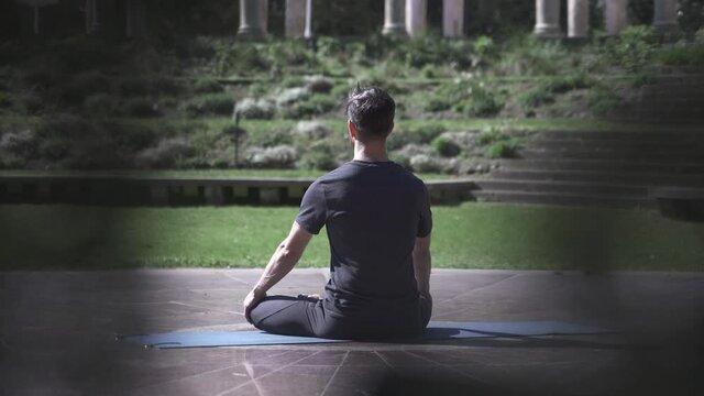 Man practices meditation and relaxation on a matt in a temple garden - Spiritual and healthy morning yoga routine