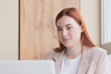 Close-up photo of a red haired business woman smiling while sitting at a computer, got a satisfactory result