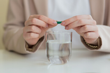 the woman's hands open the tablet in half, and dilute the medicine with a glass of water