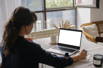White screen on laptop. Mockup. Young woman working remotely on laptop computer at cozy home office