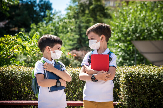 two boys, schoolchildren in black school uniforms with backpacks in a medical mask go to school independently, hold hands, friendship concept, study concept during coronavirus, back to school