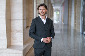 Young business man in black suit standing on the street near modern office building. Portrait.