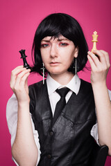 Young Citizen with Black Hair, White Shirt and Black Tie Stands Before a Pink Background and Measures the Power of Chess Pieces