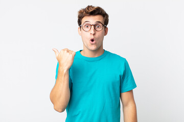 young handsome man looking astonished in disbelief, pointing at object on the side and saying wow,...