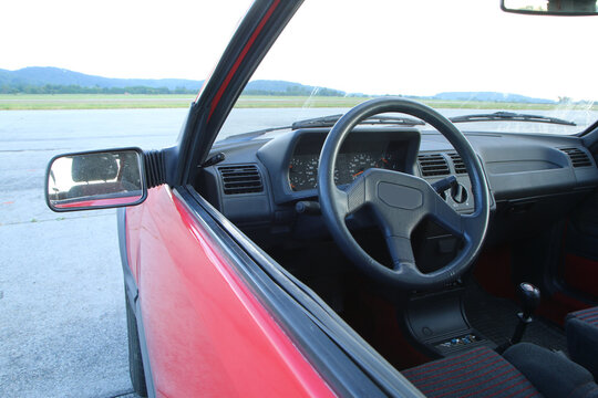The interior of the classic young timer car from the eighties. The steering wheel and dashboard are visible through the side window. 