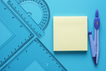 A picture of geometry set with copyspace sticky note on blue background.