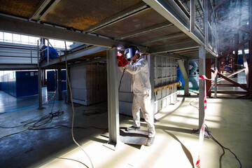  Welder in white suit works in Kazturboremont (KTR) plant workshop. Welding of metal podium construction. Atyrau,Kazakhstan.