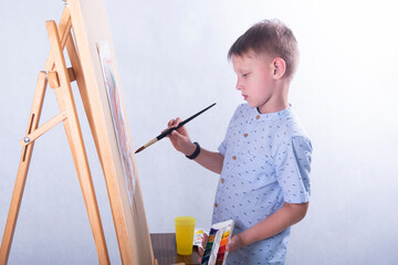 A boy artist of school age in the studio on a white background with a brush in his hand and a...