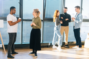 Side view of African American male posing with young woman colleague looking at camera, selective focus. Group of coworkers spending time together chatting and discussing new projects on background.