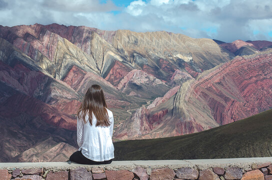 Rear view of a woman sitting on a wall looking at mountain landscape, El Hornacal, Jujuy, Argentina