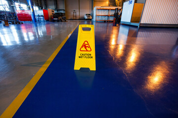 Atyrau, Kazakhstan - May 21,2012: Flowserve company modern plant. Safety caution wet floor sign on blue concrete floor. Yellow safety stripes and reflections of lights.