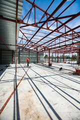 Naklejka premium Construction of new industrial building of ventilator's plant. Assembling steel structure. One element on concrete floor. Worker on background, blue sky.