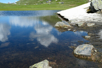 View of a lake in the mountains. Firn at the water's edge in the Alps. Pastures in the background.