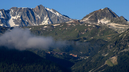 Mountain landscape. Snow-capped rocky peak with clouds and fog around.