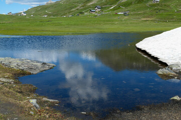 View of a lake in the mountains. Firn at the water's edge in the Alps. Pastures in the background.